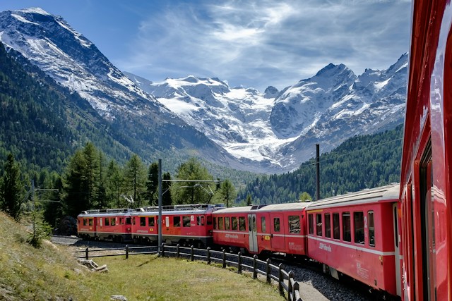 Dlaczego Szwajcarzy wybierają pociągi do podróżowania? Zdjęcie przedstawia pociąg na tle gór (Alpy) w Szwajcarii (Photo by Andreas Stutz on Unsplash)